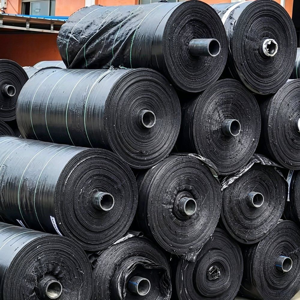 Stacked rolls of black woven weed mat in a warehouse