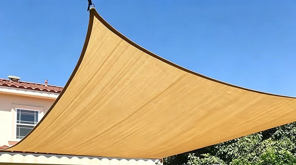 Sand coloured triangle mesh shade net sail over a garden on a sunny day