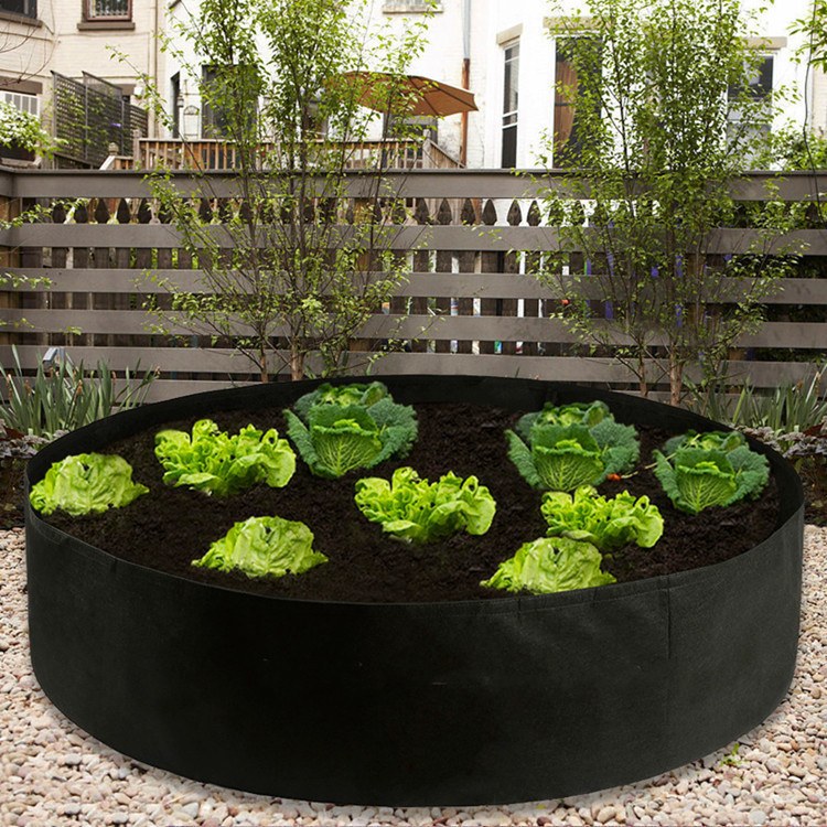 round felt raised bed planted with lettuce beside a timber fence
